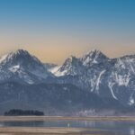 Sunset over the Bavarian Alps with snow-capped peaks reflected in a tranquil lake.