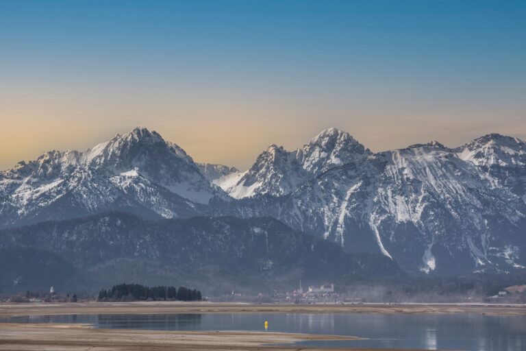Sunset over the Bavarian Alps with snow-capped peaks reflected in a tranquil lake.