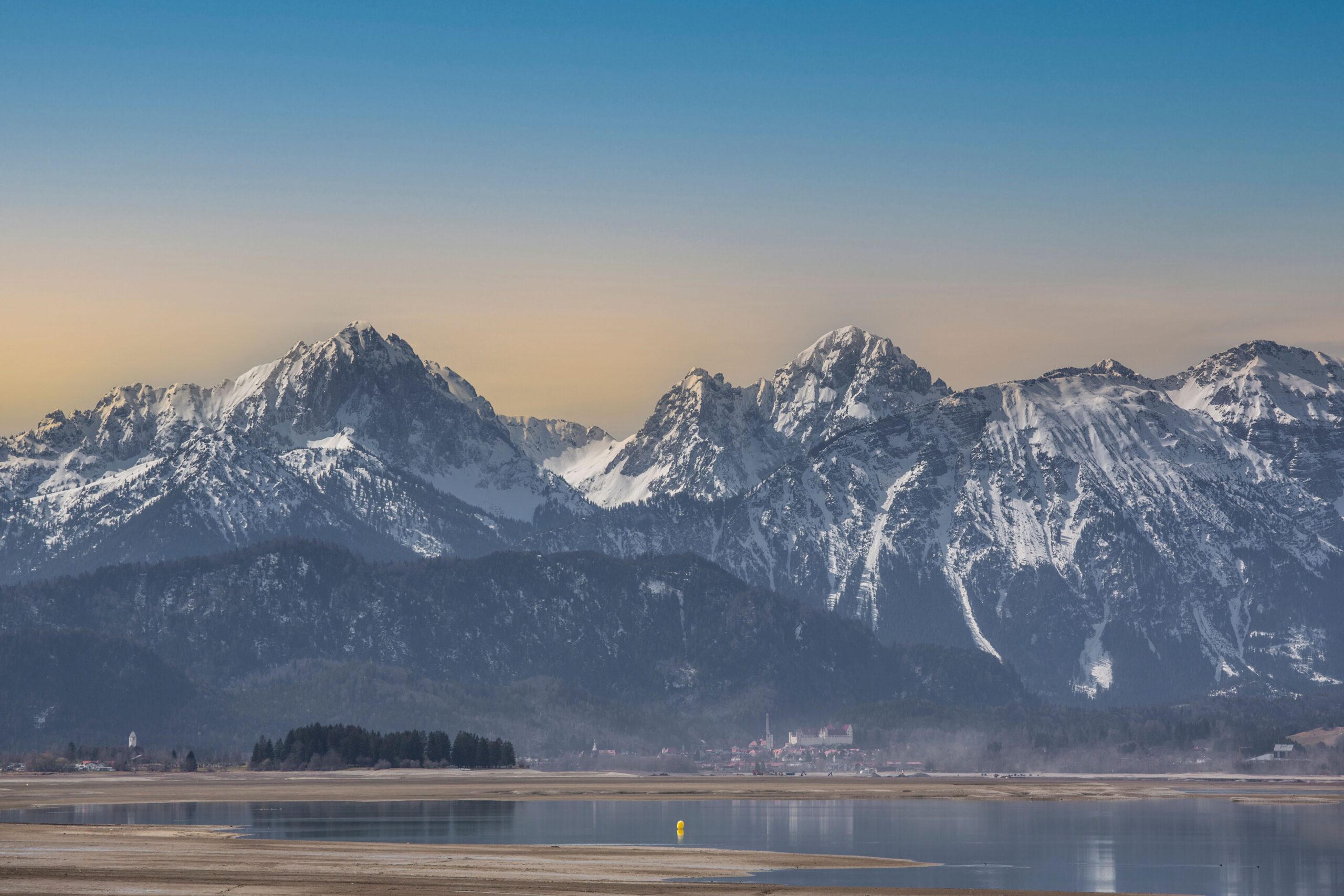 Sunset over the Bavarian Alps with snow-capped peaks reflected in a tranquil lake.